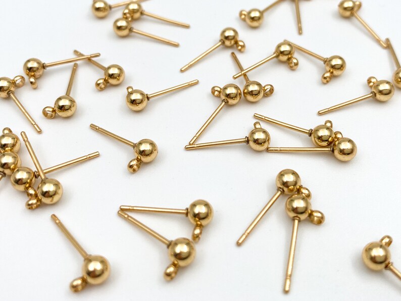 May include: A collection of gold-toned earring findings with a single ball or two balls at the end of each post.