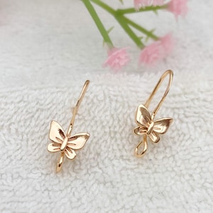 May include: A pair of gold butterfly earrings with a simple design. The earrings are made of a thin wire and have a small butterfly charm at the end.