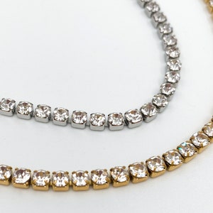 May include: Two delicate necklaces with a single row of clear cubic zirconia stones. One necklace is silver and the other is gold.