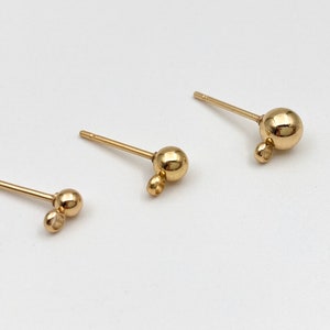 May include: Three gold-toned earring posts with a small ball at the end of the post and a larger ball at the end of a small loop.