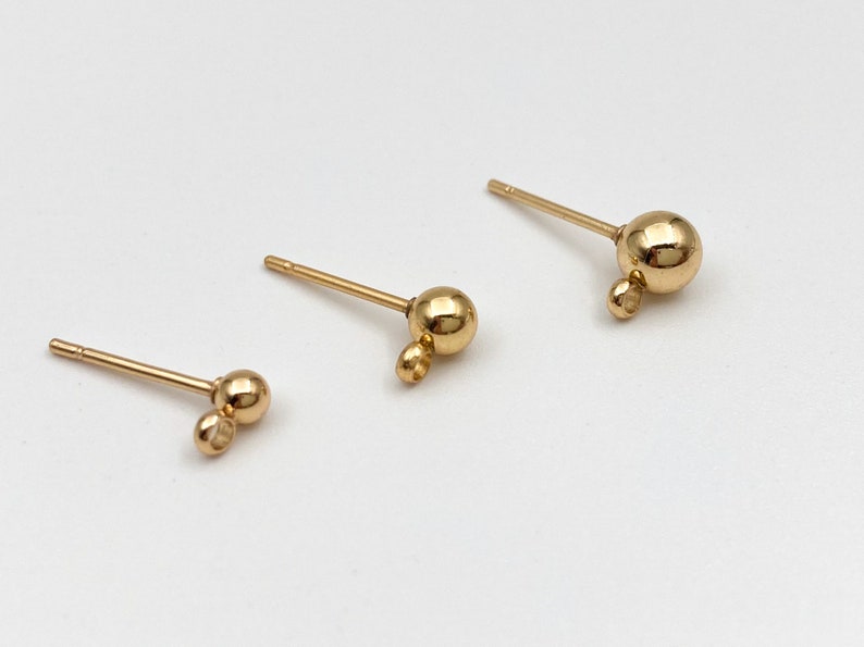 May include: Three gold-toned earring posts with a small ball at the end of the post and a larger ball at the end of a small loop.