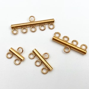 May include: Four gold-toned metal connector pieces for jewellery making. Each piece has a straight bar with multiple loops for attaching chains or cords.