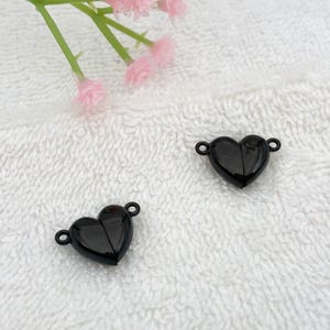 May include: Two black heart-shaped clasps with a shiny finish. The clasps are open and ready to be attached to a necklace or bracelet.