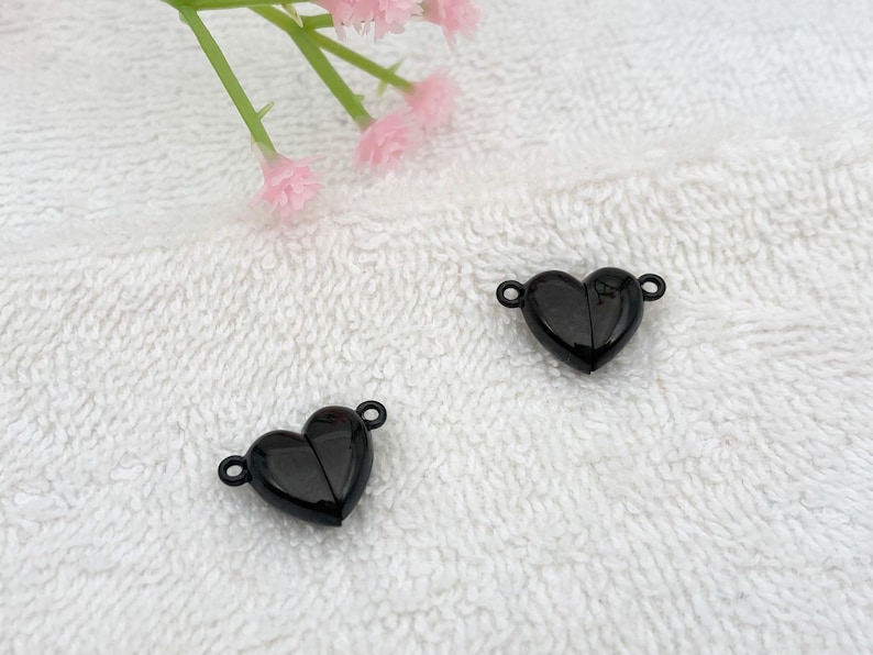 May include: Two black heart-shaped clasps with a shiny finish. The clasps are open and ready to be attached to a necklace or bracelet.