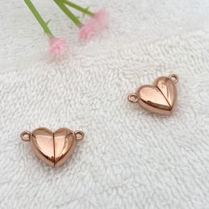 May include: Two rose gold heart-shaped magnetic clasps for jewelry making. The clasps are made of metal and have a shiny finish.