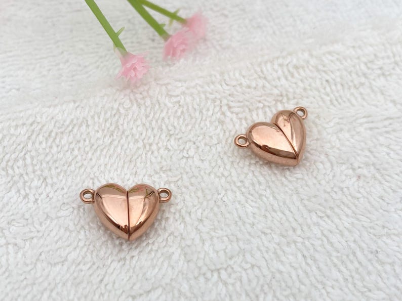 May include: Two rose gold heart-shaped magnetic clasps for jewelry making. The clasps are made of metal and have a shiny finish.