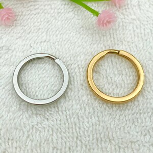 May include: Two key rings, one silver and one gold, are shown on a white textured surface.