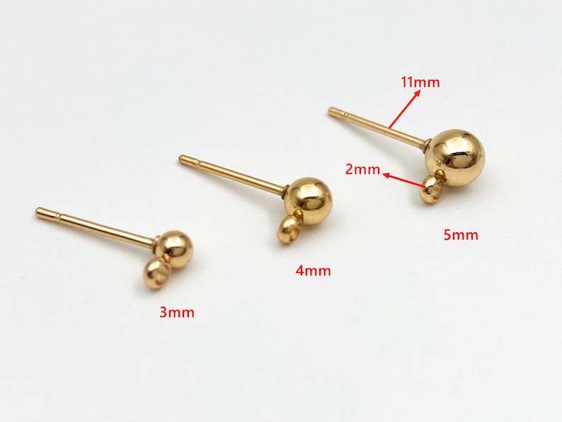 May include: Three gold-toned earring findings with different sized ball charms. The smallest finding is 3 mm long, the middle finding is 4 mm long, and the largest finding is 11 mm long.