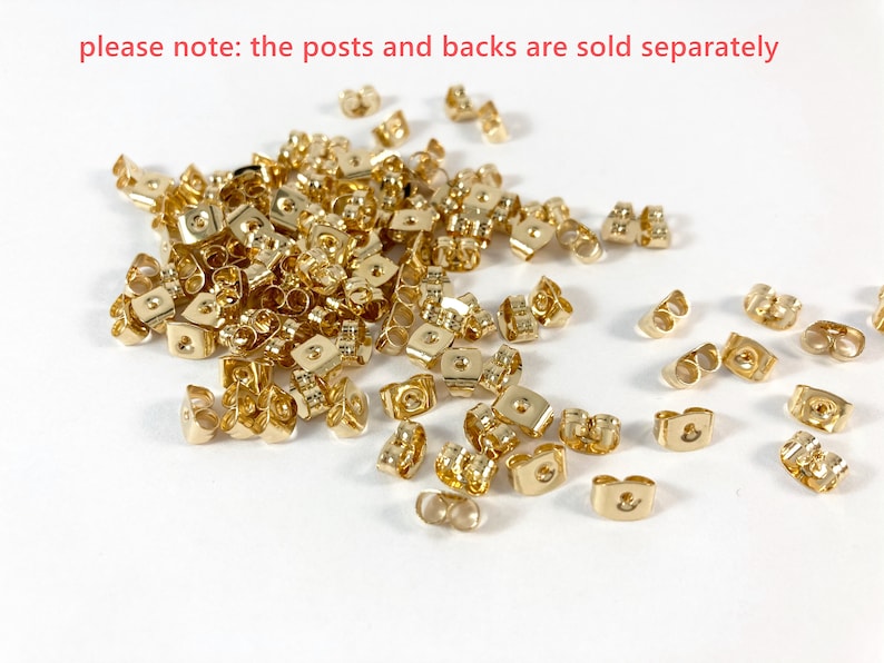 Op de afbeelding: Een grote stapel gouden oorbelruggen. De ruggen zijn van metaal en hebben een kleine lus aan de bovenkant. De tekst "please note: the posts and backs are sold separately" is zichtbaar bovenaan de afbeelding.