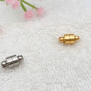 May include: Two magnetic clasps for jewelry, one gold and one silver. The clasps are round and have a small ball on each end.