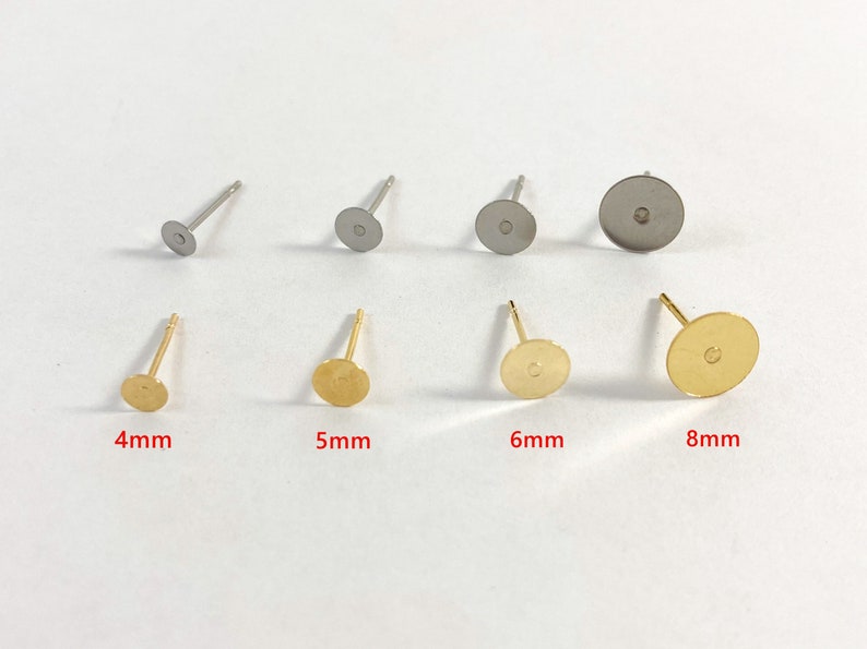 Op de afbeelding: Vier oorbel achterkanten in verschillende maten: 4 mm, 5 mm, 6 mm en 8 mm. De oorbelpennen zijn goudkleurig en de achterkanten zijn zilverkleurig.