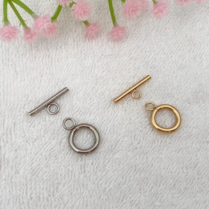 May include: Two metal toggle clasps, one silver and one gold. Each clasp has a round ring attached.
