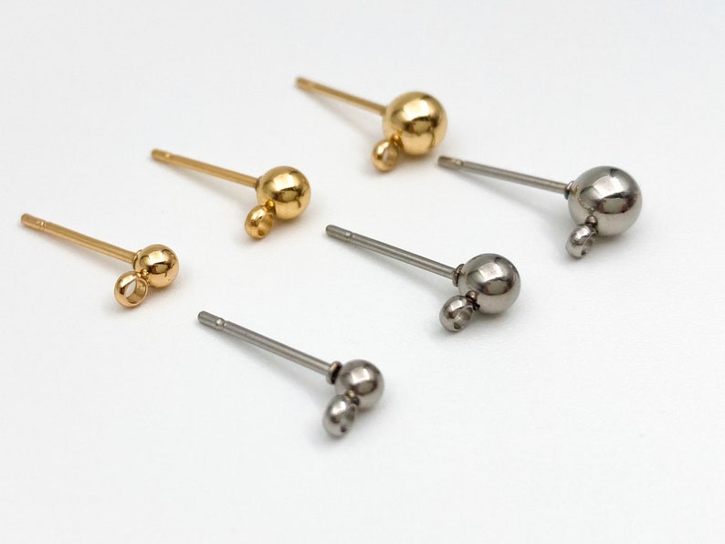 May include: Four pairs of earring findings with a small ball and a loop at the end. Two pairs are gold and two pairs are silver.