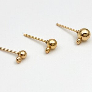 May include: Three gold-toned earring posts with different sized ball charms. The smallest charm is a double ball, the middle charm is a single ball, and the largest charm is a single ball.