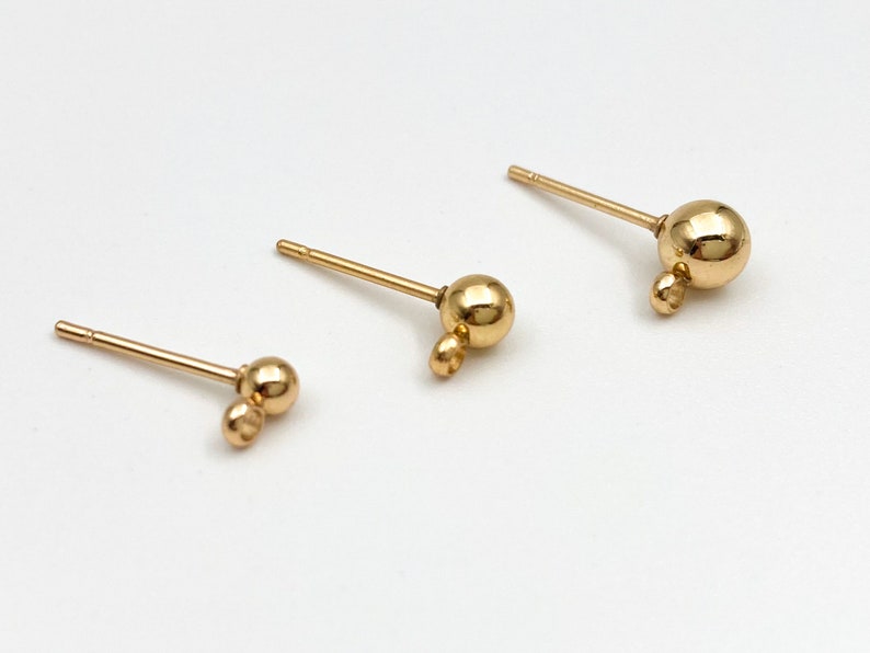 May include: Three gold-toned earring posts with different sized ball charms. The smallest charm is a double ball, the middle charm is a single ball, and the largest charm is a single ball.