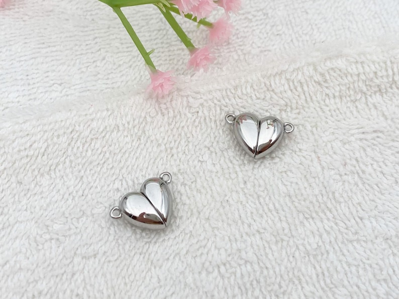 May include: Two silver heart-shaped magnetic clasps for jewelry making. The clasps are open and ready to be attached to a necklace or bracelet.