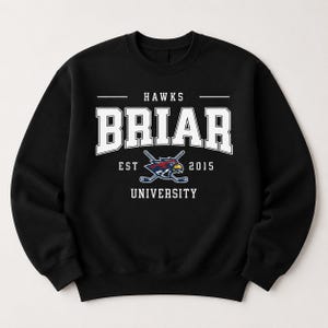 Op de afbeelding: Zwart sweatshirt met de tekst "HAWKS BRIAR UNIVERSITY EST 2015" in witte blokletters. Het ontwerp bevat een logo van gekruiste hockeysticks en een havik. De sweatshirt heeft een ronde hals.