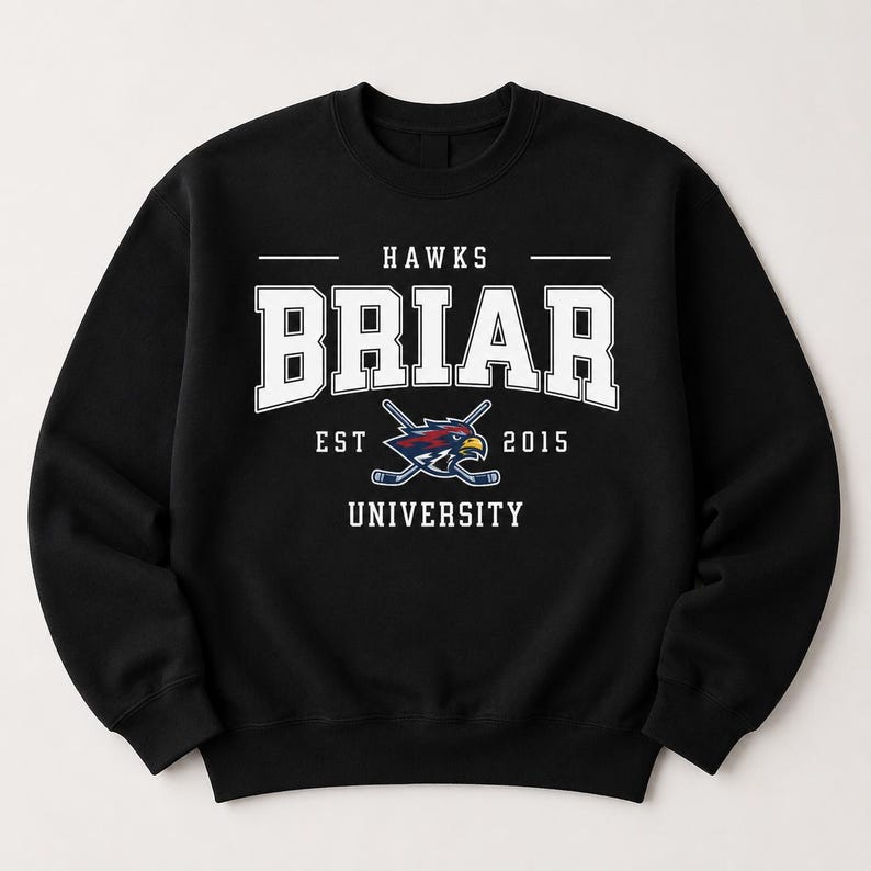Op de afbeelding: Zwart sweatshirt met de tekst "HAWKS BRIAR UNIVERSITY EST 2015" in witte blokletters. Het ontwerp bevat een logo van gekruiste hockeysticks en een havik. De sweatshirt heeft een ronde hals.
