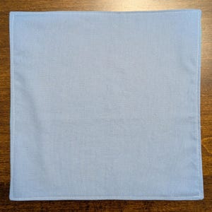 May include: A plain light blue fabric square with white stitching around the edges.