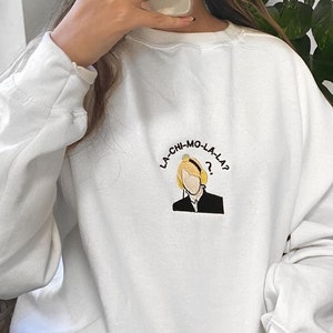 Puede incluir: Sudadera blanca con un diseño bordado en amarillo y negro de una persona con auriculares y el texto "LA-CHI-MO-LA-LA?"