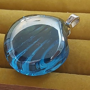 May include: A blue glass heart pendant with a silver bail. The glass has a swirling pattern of blue and white.