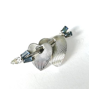 May include: A silver brooch with two hearts and an arrow, decorated with blue and clear rhinestones.