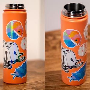 May include: Orange insulated water bottle with a silver lid. The bottle is decorated with colorful stickers, including a rainbow-colored caterpillar, a die with a ghost, and a blue bug. The bottle is on a wooden surface.