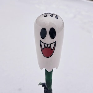 May include: White ghost-shaped gear shift knob with black eyes, a red mouth, and black numbers 2, 4, and 6 on the top.