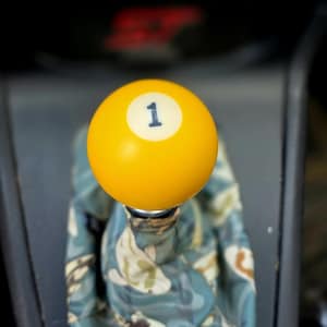 May include: A yellow billiard ball shift knob with the number 1 in black on a white circle. The shift boot has a blue, green, and white koi fish pattern.