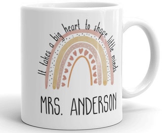 Puede incluir: Taza de café de cerámica blanca con un diseño de arcoíris y el texto "Se necesita un gran corazón para moldear las mentes pequeñas" y "MRS. ANDERSON".
