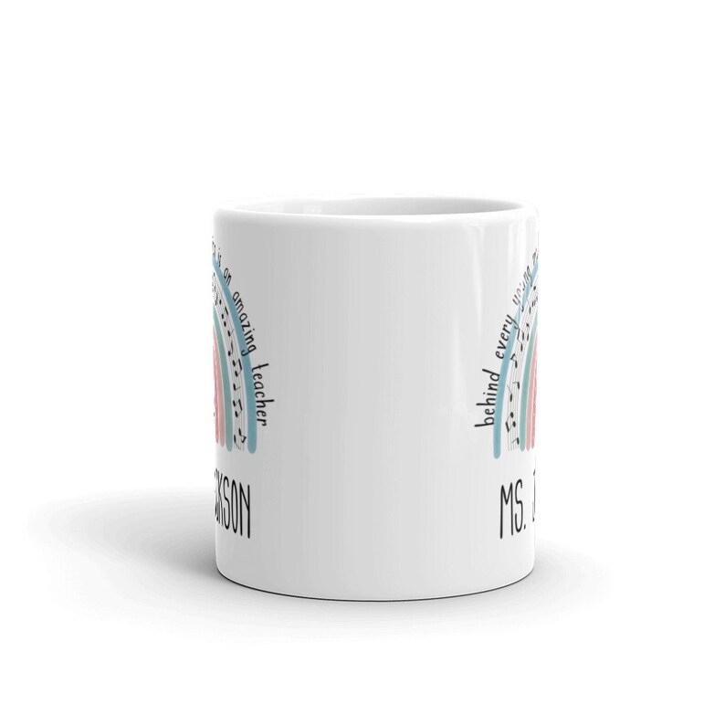 Może przedstawiać: Biały ceramiczny kubek do kawy z wzorem tęczy i tekstem "There is an amazing teacher behind every unicorn" oraz "MS. JACKSON".
