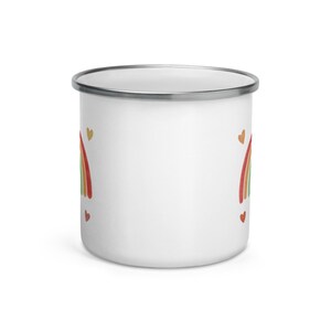 May include: White enamel mug with a rainbow and hearts design. The rainbow is in shades of red, orange, yellow, green, and blue. The hearts are in shades of gold and red.