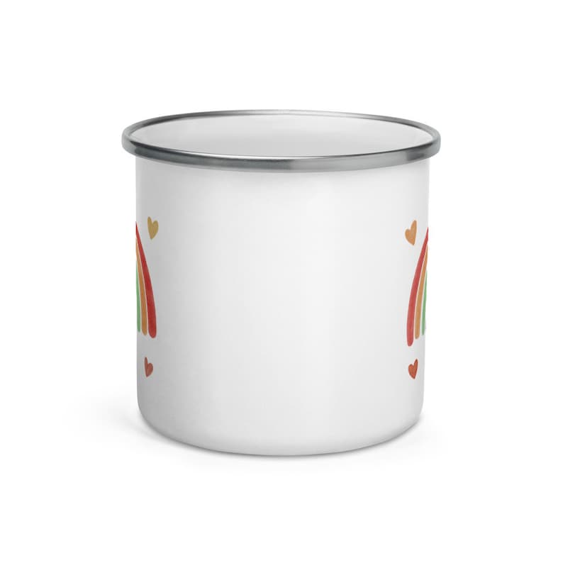 May include: White enamel mug with a rainbow and hearts design. The rainbow is in shades of red, orange, yellow, green, and blue. The hearts are in shades of gold and red.