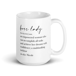 May include: A white ceramic mug featuring the words "boss lady" in a script font. The mug includes a definition of "boss lady" and the name "Nicole". The mug has a curved handle.