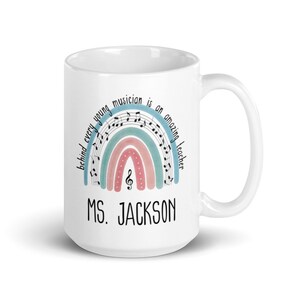 Może przedstawiać: Biały kubek ceramiczny z wzorem tęczy ozdobionym nutami i tekstem "Behind every young musician is an amazing teacher." Kubek ma r&oacute;wnież nadrukowane imię "MS. JACKSON".