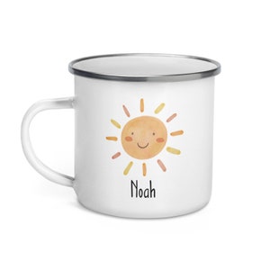 K&ouml;nnte beinhalten: Wei&szlig;e Email Tasse mit einer l&auml;chelnden Sonnenillustration und dem Namen "Noah" darunter gedruckt.