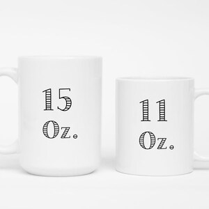 Może przedstawiać: Dwa białe ceramiczne kubki z czarnym tekstem. Większy kubek ma napis "15 oz.", a mniejszy kubek ma napis "11 oz."