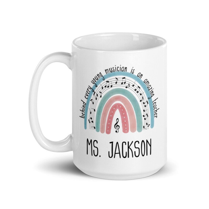Może przedstawiać: Biały kubek ceramiczny z wzorem tęczy i nutami. Tekst "Behind every young musician is an amazing teacher" jest napisany wok&oacute;ł tęczy. Tekst "Ms. Jackson" jest napisany pod tęczą.
