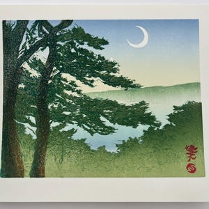 May include: A woodblock print depicting a crescent moon in a blue sky above a misty lake.  The lake is surrounded by green trees and hills.  The print is signed in red ink in the lower right corner.