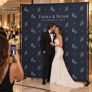 May include: A large navy blue wedding step and repeat backdrop featuring a repeating pattern of white leaf illustrations, small four-pointed stars, and the monogram EN. The text reads EMMA & NOAH and SEPTEMBER 12, 2026 in white lettering.