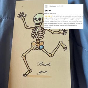 May include: A tan thank you postcard featuring a cartoon skeleton in a running pose. The skeleton is drawn in black and tan, with the words "Thank you" in elegant script below. The card has a UV high gloss finish.