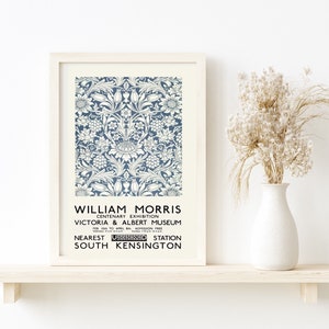 May include: A white framed poster with a blue and white floral pattern. The poster advertises a William Morris Centenary Exhibition at the Victoria & Albert Museum in London, England. The text on the poster reads "William Morris Centenary Exhibition Victoria & Albert Museum Feb 10th to April 8th Admission Free Nearest Underground Station South Kensington".