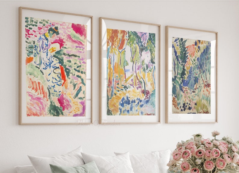 May include: Three framed abstract paintings with colourful brushstrokes and a landscape theme. The paintings are in a white room with a bouquet of pink flowers in the foreground.