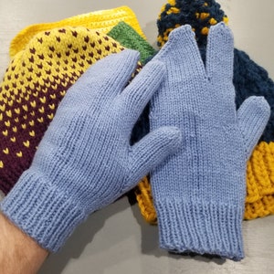 Puede incluir: Un par de guantes sin dedos de punto azul. Los guantes están hechos de un hilo suave y texturizado y tienen un diseño simple y clásico.