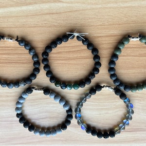 May include: Five beaded bracelets with black lava rock beads and different coloured accent beads. The bracelets have silver clasps.