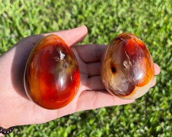 以下が含まれることがあります： 赤い、オレンジ、白のパターンが入ったカーネリアンクリスタルエッグ2個。もう1つは、オレンジと白の落ち着いたパターンです。