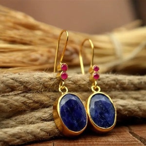 May include: A pair of gold earrings with blue oval-shaped gemstones and small pink accents.