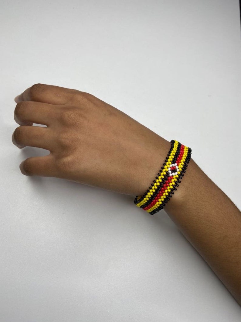 May include: A beaded bracelet with black, yellow, and red stripes and a white circle in the center.