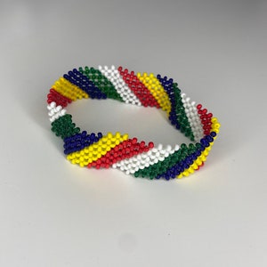 May include: A colorful beaded bracelet with a diagonal pattern of green, blue, yellow, red, and white beads.
