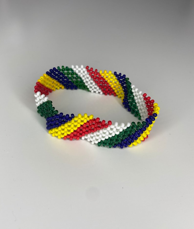 May include: A colorful beaded bracelet with a diagonal pattern of green, blue, yellow, red, and white beads.